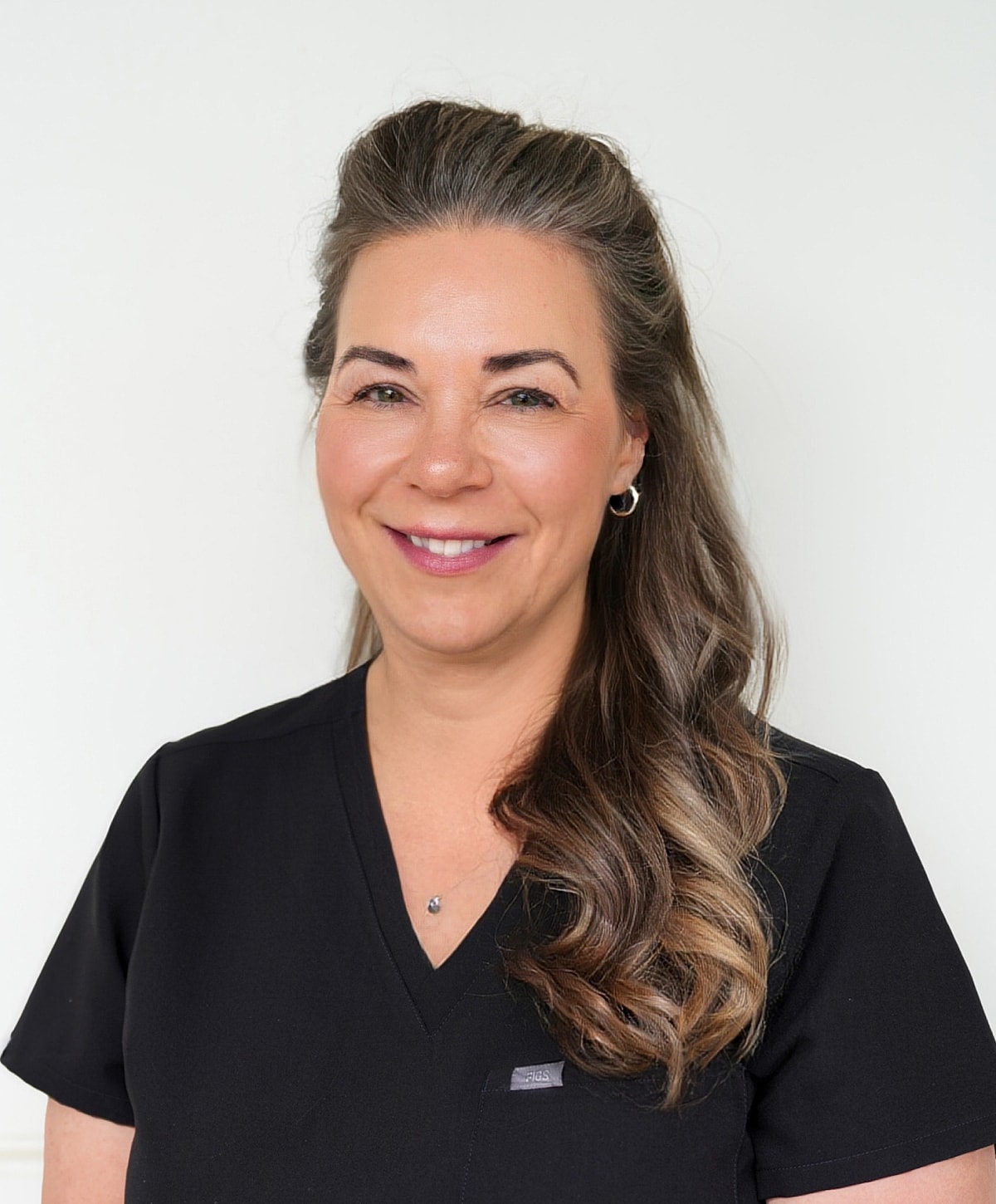 Smiling woman in black scrubs against white background.