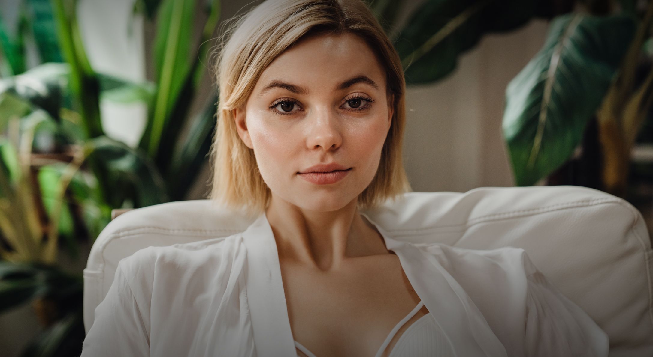 Woman sitting softly smiling among indoor plants.