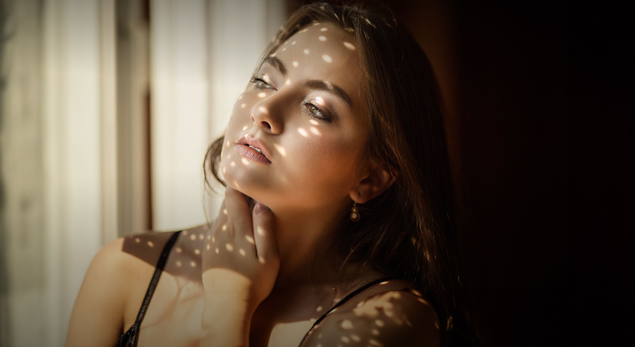 Woman illuminated by patterned sunlight indoors.